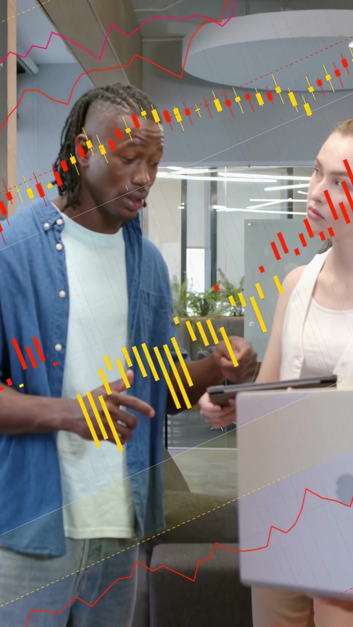 Vertikal video: Mann peker på nettbrett som viser datadiagrammer for virksomheten, mens en kvinne med bærbar PC nikker.