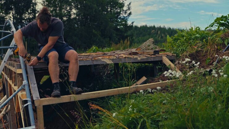 Uomo che utilizza un utensile elettrico mentre svolge lavori agricoli in un'area rurale della Norvegia, circondato da vegetazione di campagna e terreni coltivati