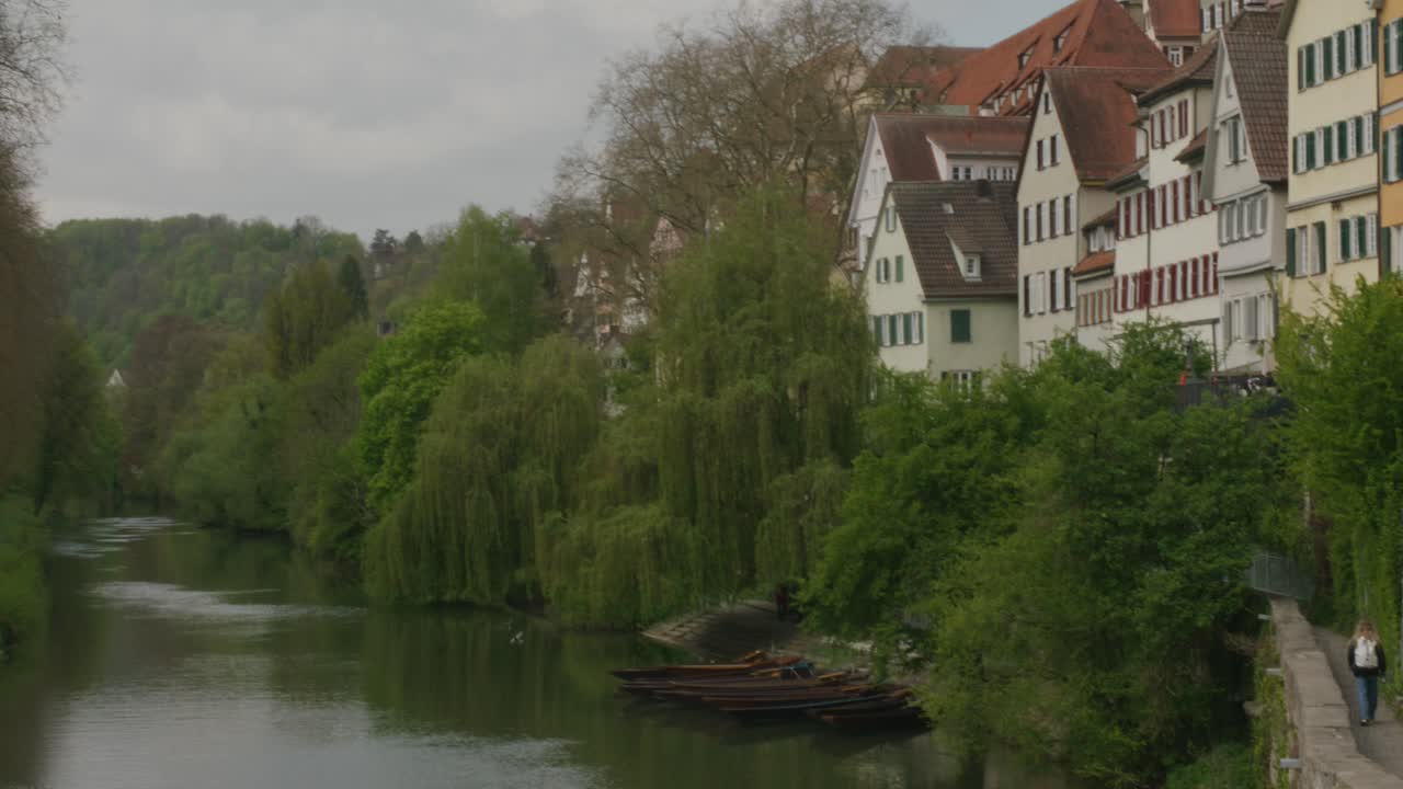 Turista che cammina lungo un sentiero che si affaccia sul fiume mentre gli uccelli volano vicino nel centro storico di Tubinga in Baviera a mezzogiorno, Germania, Europa, ripresa panoramica