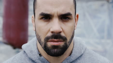 close-up view of handsome bearded sportsman looking with serious expression at the camera outdoors an abandoned factory on a cloudy morning