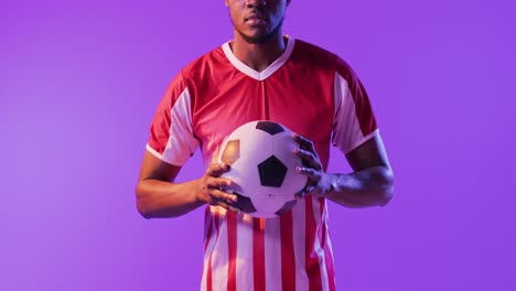 Portrait-of-african-american-male-soccer-player-with-football-over-neon-pink-lighting