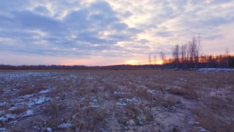 low aerial drone view of vast frozen field covered with light snow, sunset