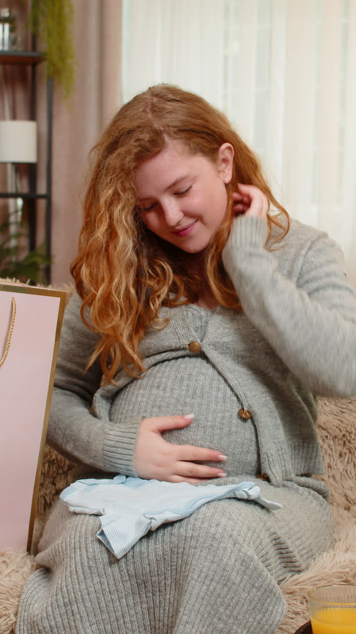 Pregnant woman unpacking shopping bags with baby clothes excited and satisfied with new purchases