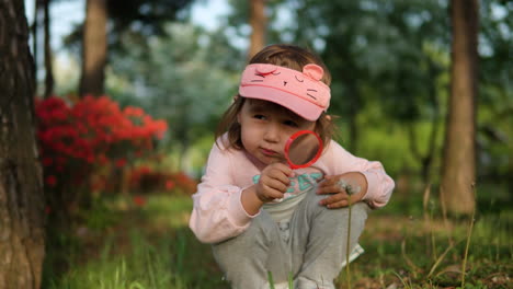 little girl in cute sunvisor playing and looking on dandelion through magnifying glass