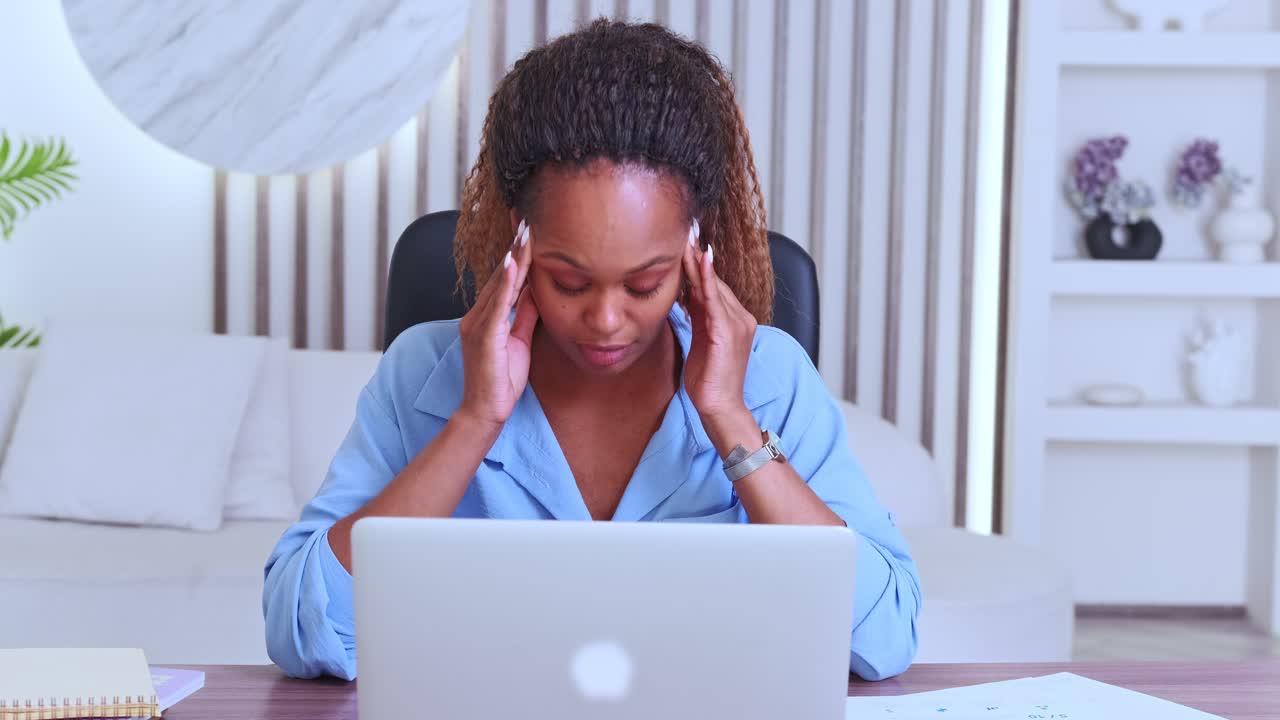 Young tired african american woman feels headache due to working with laptop
