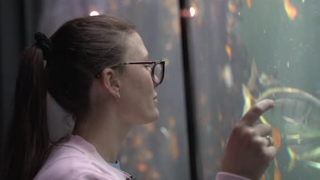 primer plano de una mujer mirando y tocando el cristal en el acuario mientras los peces nadan junto a ella