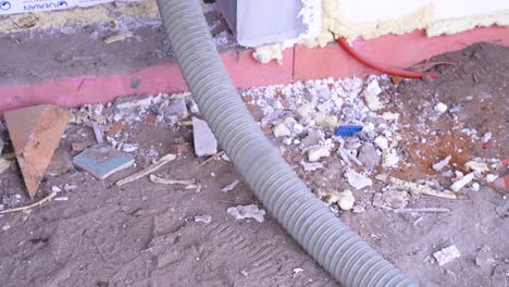 insulation material transport hose lies beside broken material fragments near building foundation