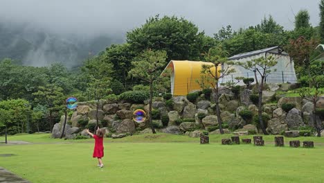 active little girl runs after blowing soap bubbles in green mountain park lawn - wide angle