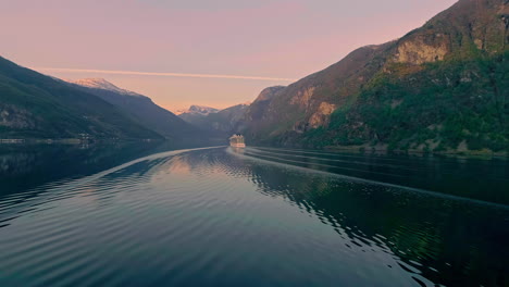 drone wide shot showing slowly cruising cruise ship on norweguian fjord during sunrise