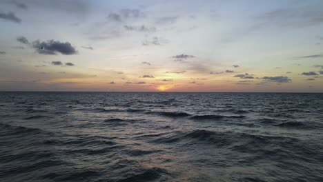 Low-ocean-aerial:-Colorful-golden-sunrise-over-wavy-sea-to-horizon