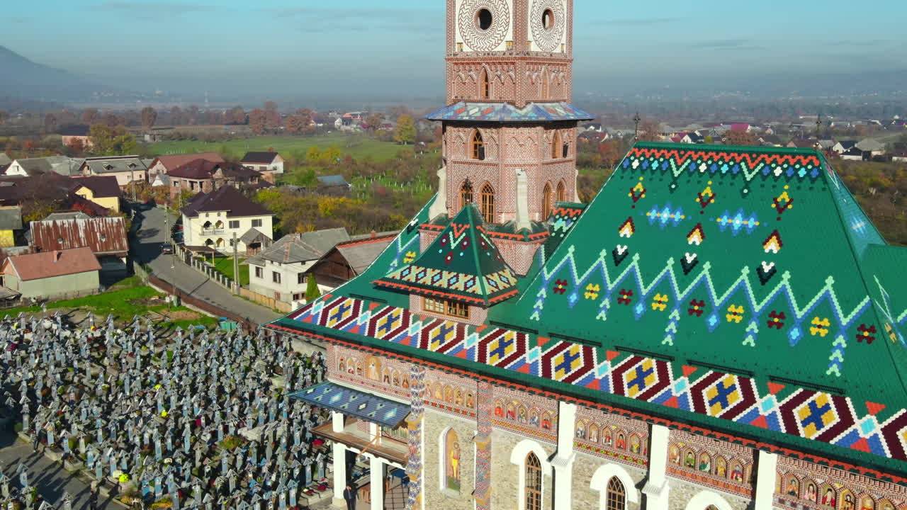 Aerial drone view of The Merry Cemetery in Sapanta, Romania. Church and multiple tombstones, visitors, residential buildings, yellowing trees