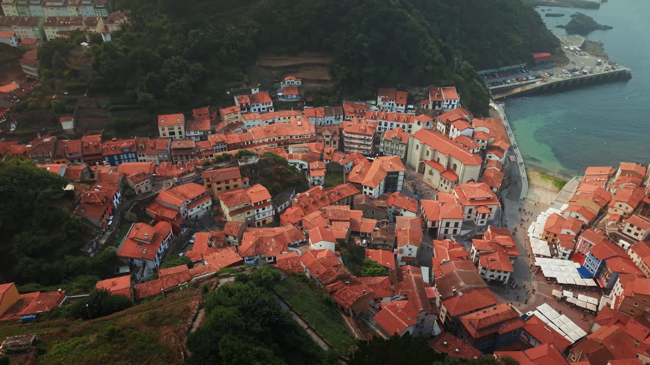 Órbita de drone revelando as casas de telhado vermelho da vila de pescadores e porto de Cudillero ao longo da costa das Astúrias, no norte da Espanha