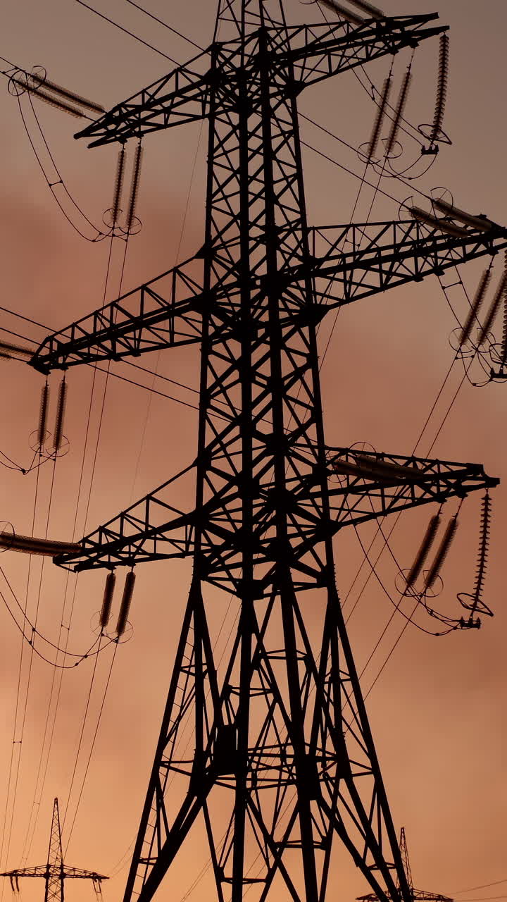 High voltage electric lines and industry. Pipes with dark smoke near the transmission electric towers at dusk. Pollution the atmosphere. View from below. Vertical video