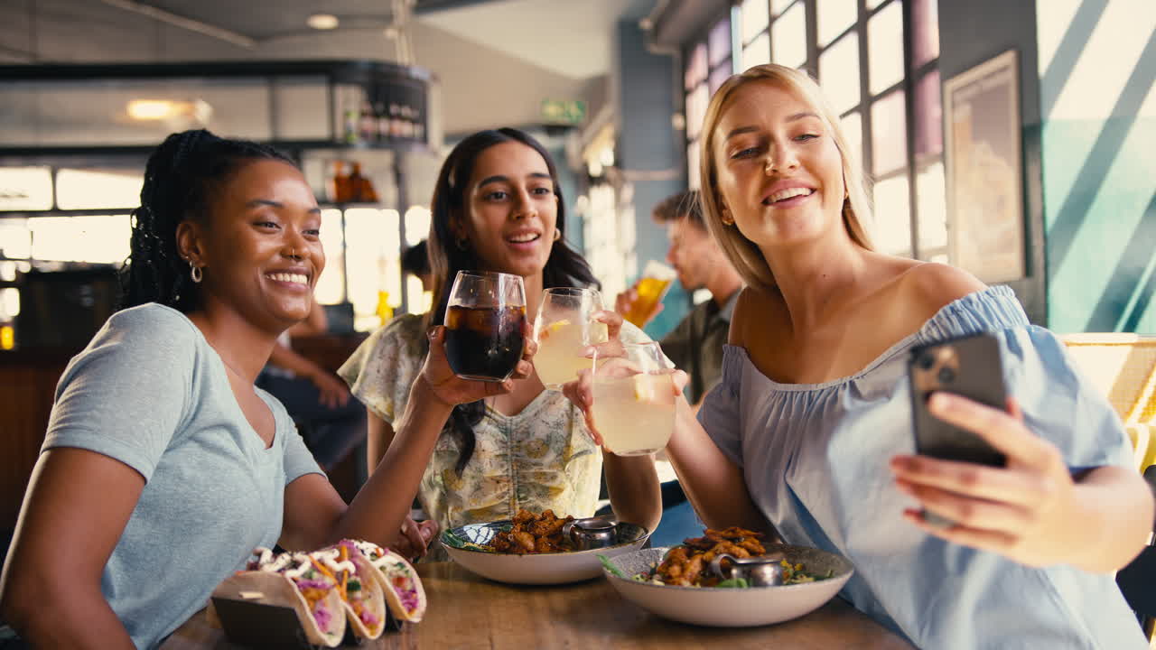 Group Of Female Friends Meeting Up In Restaurant Posing For Selfie On Mobile Phone With Food