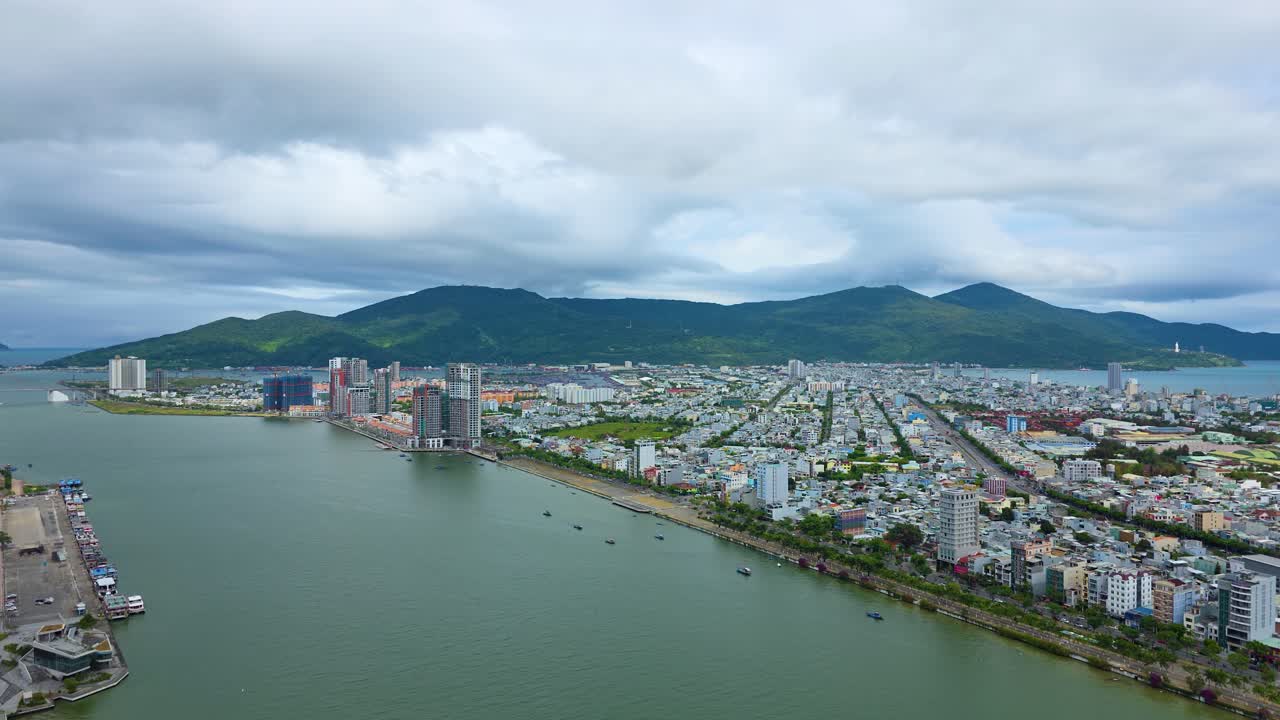 Timelapse trên không của cảnh quan thành phố Đà Nẵng dọc sông Hàn với bờ sông đô thị, các khu dân cư đông đúc và núi Sơn Trà dưới bầu trời đầy mây ấn tượng