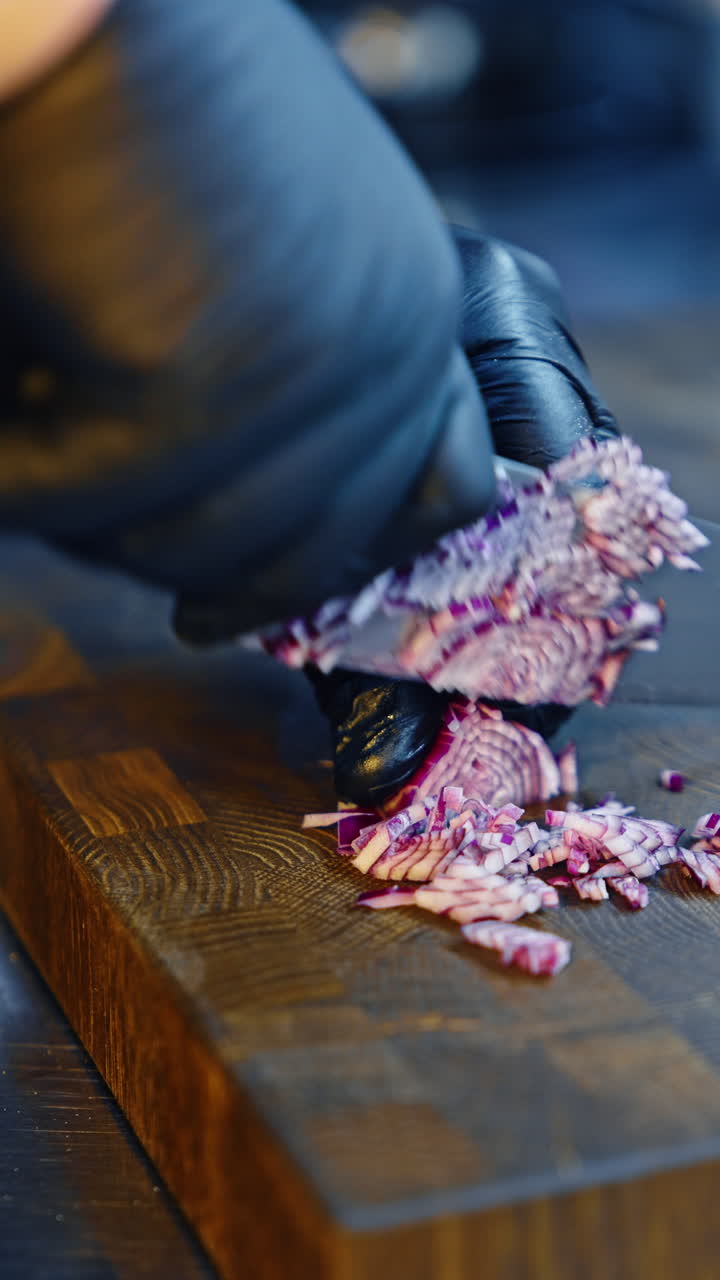 Chef cutting onions with a big knife on the wooden board. Preparing vegetables in the restaurant. Close up. Vertical video.