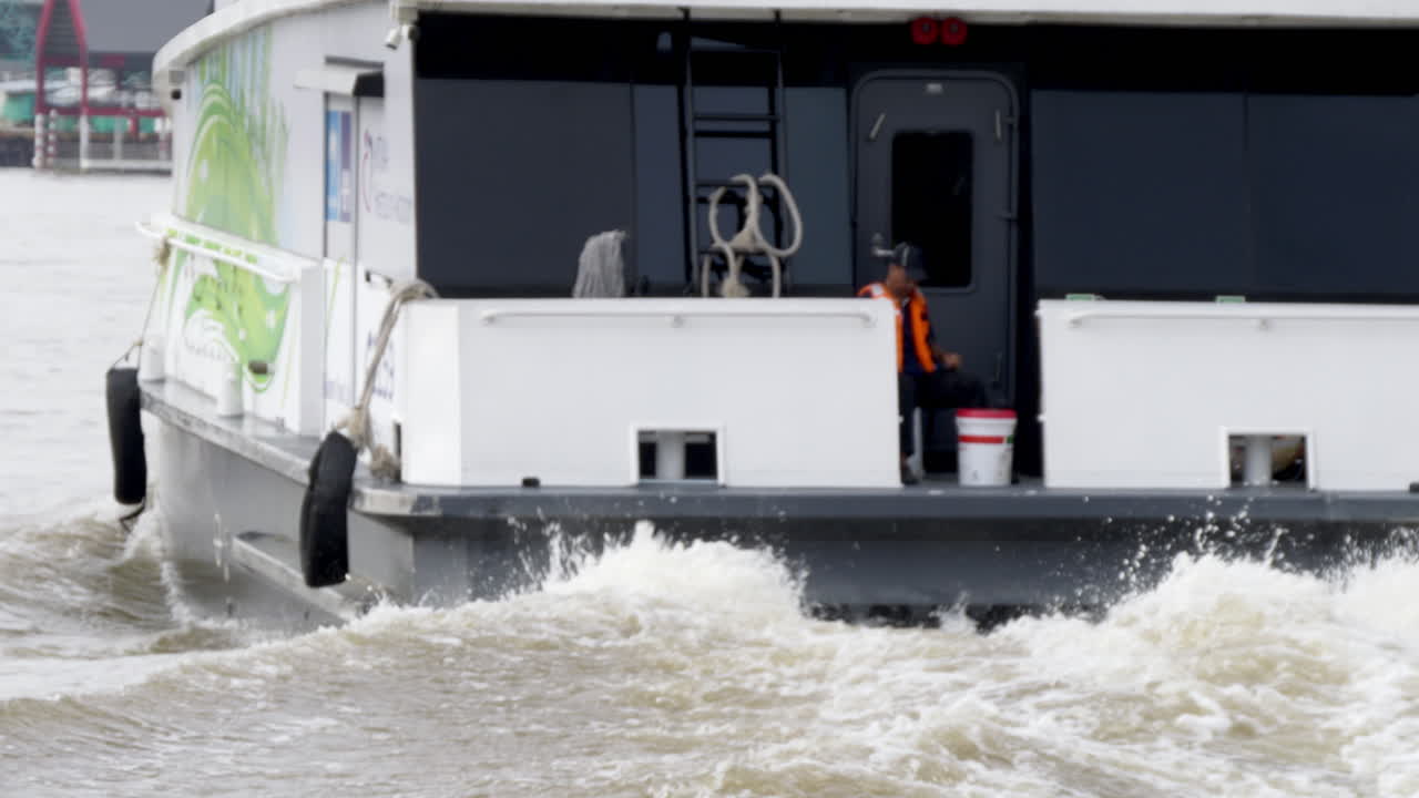 The electric speedboat's engine roars in a close-up shot as it departs the pier in Bangkok, demonstrating sustainable transportation in the vibrant city.