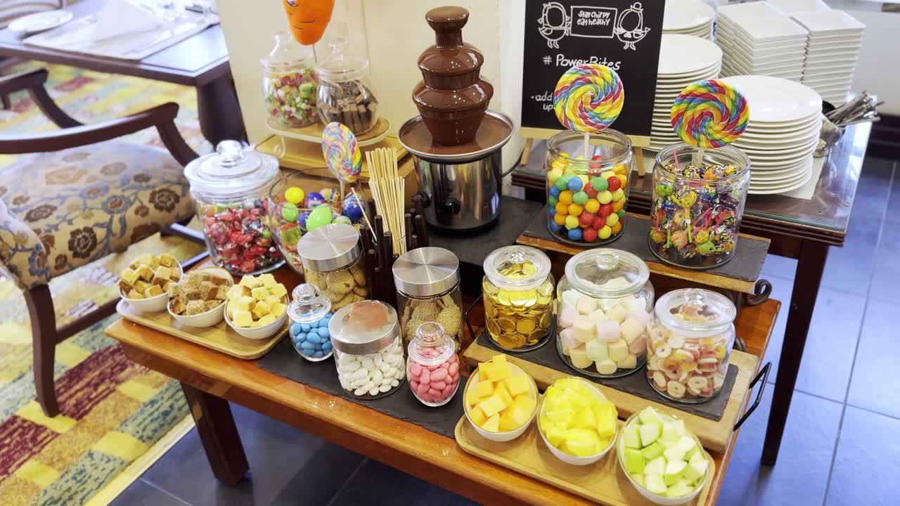 4K shot of a vibrant candy buffet with a chocolate fountain, assorted sweets, and lollipops. Ideal for party, dessert, catering, celebration, and kids-themed content.