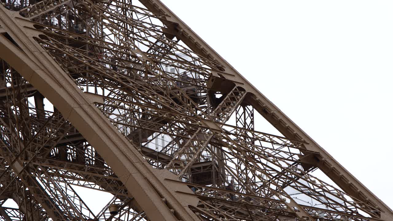 Static close-up shot captures the intricate metal lattice of the Eiffel Tower against overcast skies