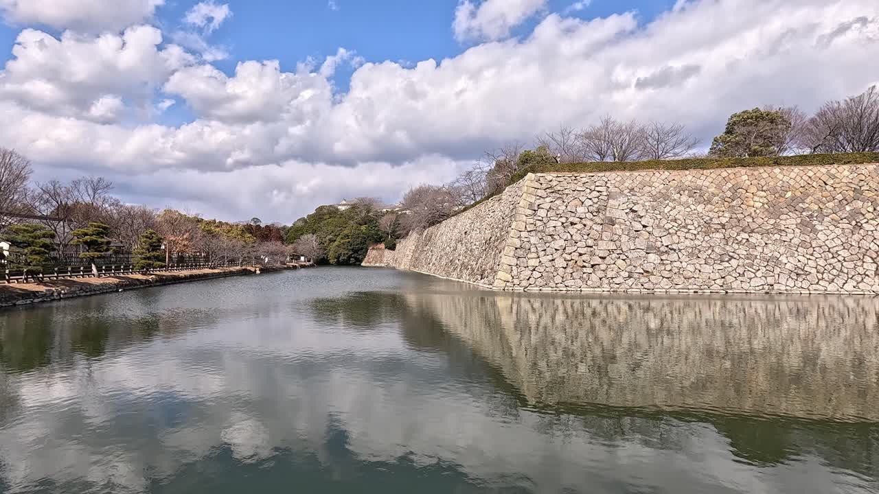 Stone walls and reflecting water in the exterior moat of Himeji Castle in Hyogo Japan under Cloudy Blue Sky . Himeji Castle in Hyogo Japan