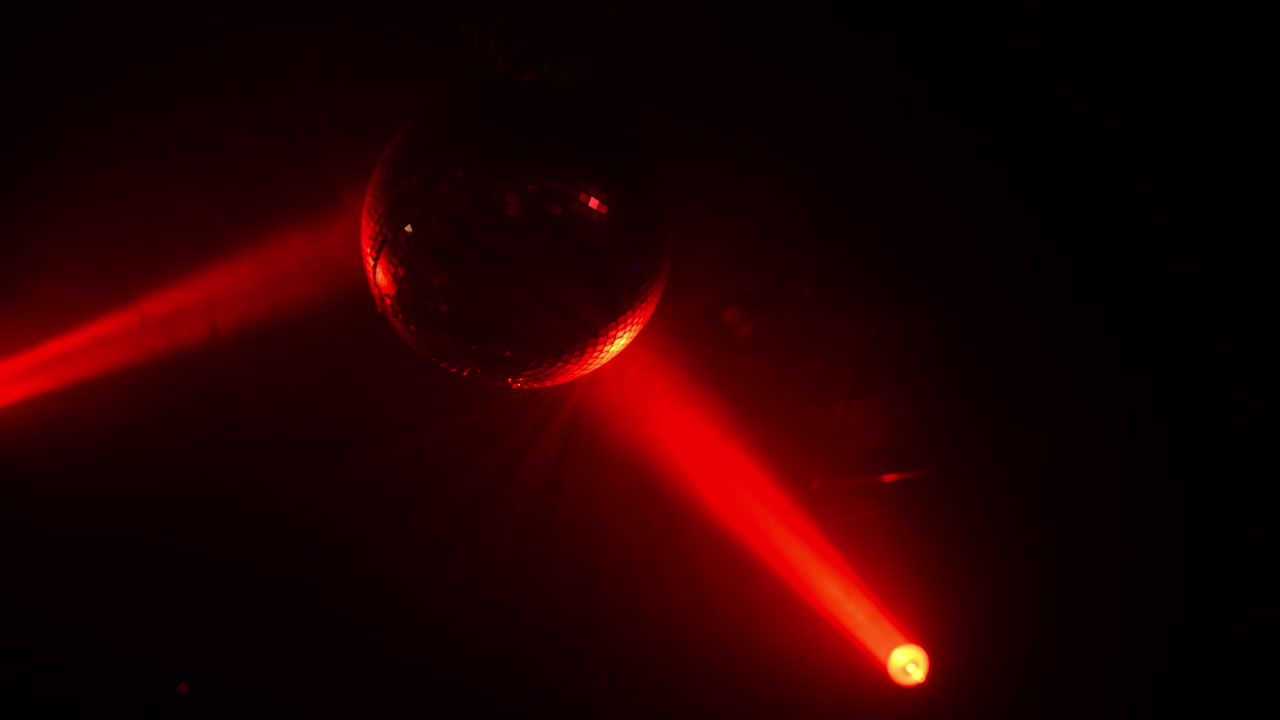 Globo de espelhos refletindo feixes de luz vermelha brilhante, criando uma atmosfera vibrante de festa dançante