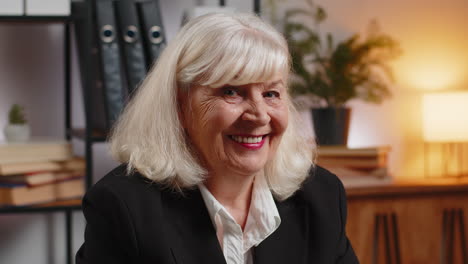 smiling senior businesswoman using laptop computer and looking at camera at home office table