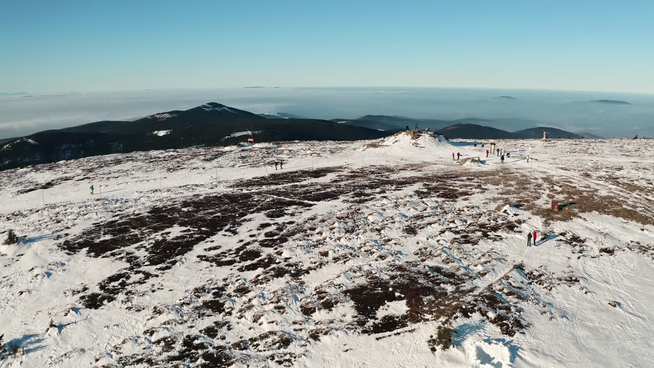 People hiking on top of czech mountain covered with snow from drone
