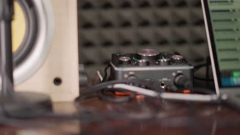 close-up of a black sound mixer with dials and knobs, placed on a desk in a recording studio. a studio monitor speaker is partially visible to the left, with an acoustic foam background