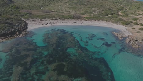 Aerial-Drone-Zooms-Out-Turquoise-beach-water-bay-at-Cala-Sa-Torreta-Spain-Travel-Destination,-natural-environment