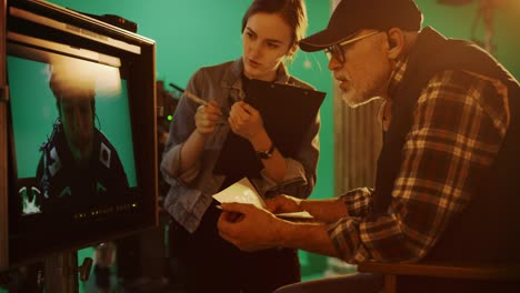 director looks at display and compares to storyboard while shooting blockbuster movie. green screen scene with actor wearing motion caption suit. film studio professional crew doing high budget movie