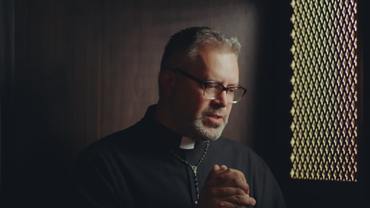Catholic Priest Praying inside of Confessional Booth in Church