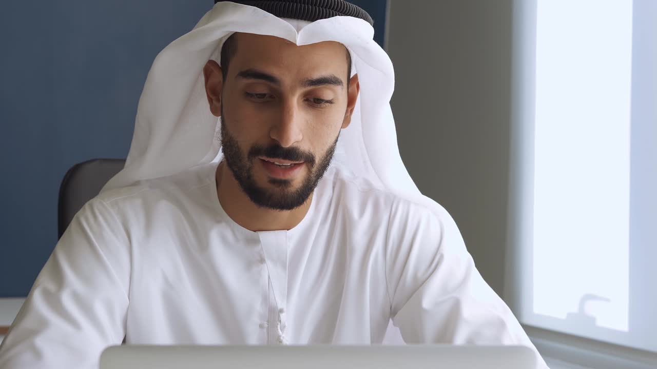 Komea mies perinteisissä vaatteissa työskentelemässä Dubain toimistossa