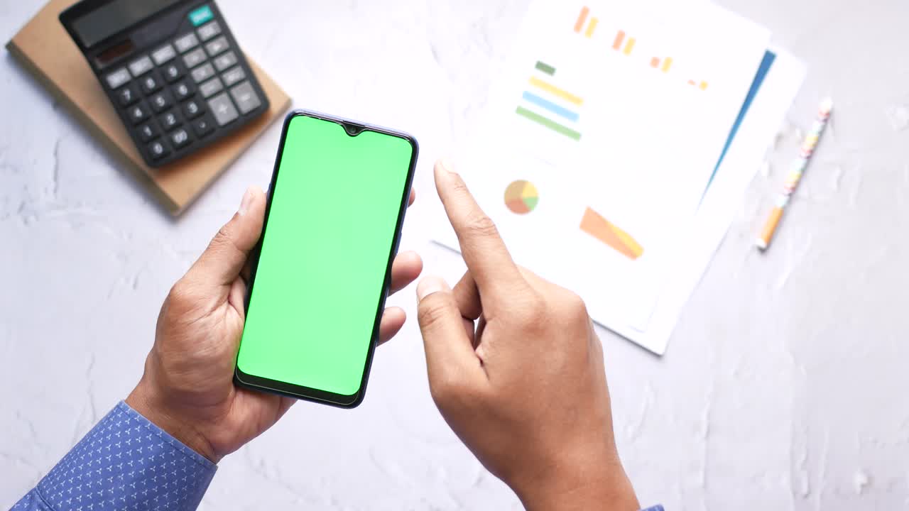 Person holding a smartphone with a green screen, surrounded by business documents and a calculator.