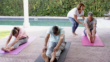 seniors practicing yoga on mats by pool, stretching and exercising together
