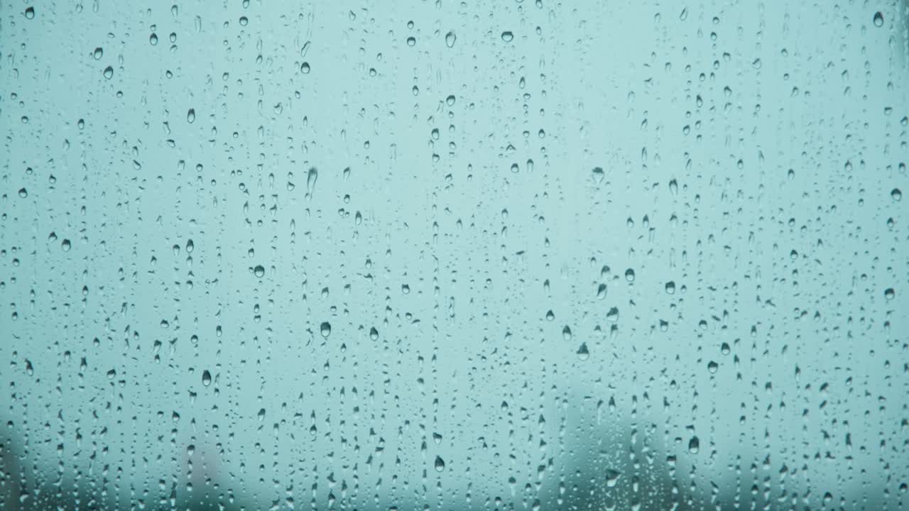 vista de cerca de las gotas de lluvia que caen por la superficie del vidrio con fondo azul. gotas de agua que caen durante las fuertes lluvias.