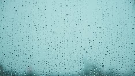 vista de cerca de las gotas de lluvia que caen por la superficie del vidrio con fondo azul. gotas de agua que caen durante las fuertes lluvias.