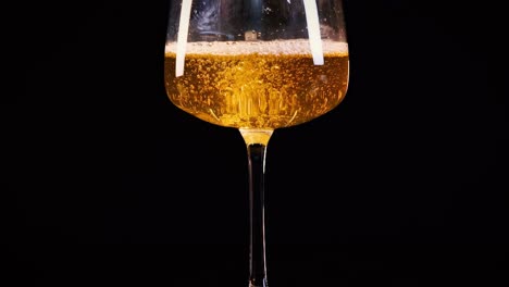close-up of a glass with golden liquid and bubbles against a dark backdrop.