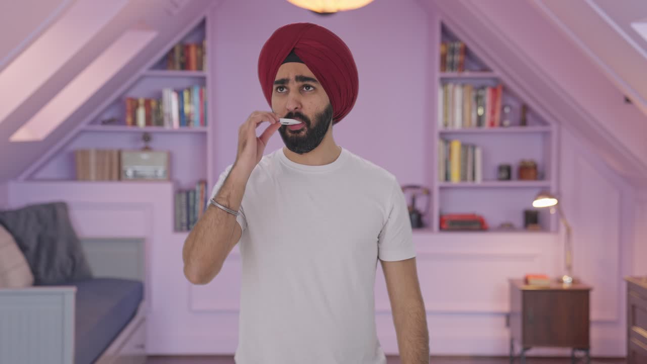 Uomo indiano Sikh malato che usa un termometro per controllare la febbre