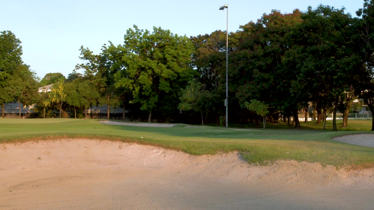 L'ombra di un golf cart attraversa un bunker di sabbia su un campo da golf verde lussureggiante