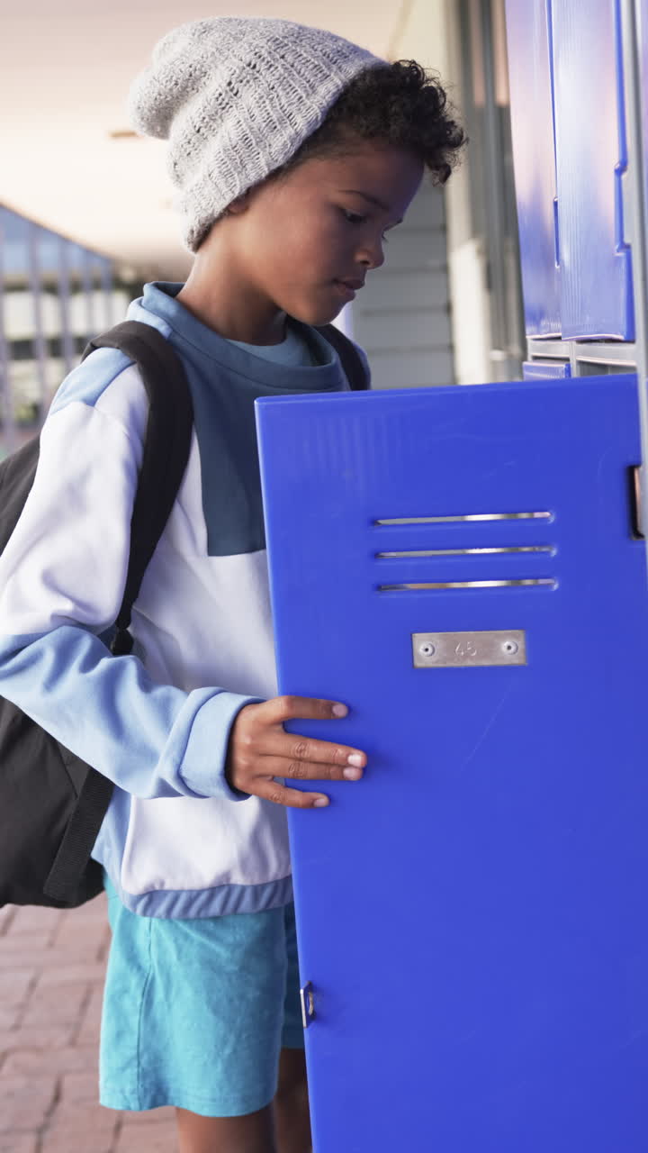 Vertical video: In school, boy with backpack opening locker, holding notebook and folder