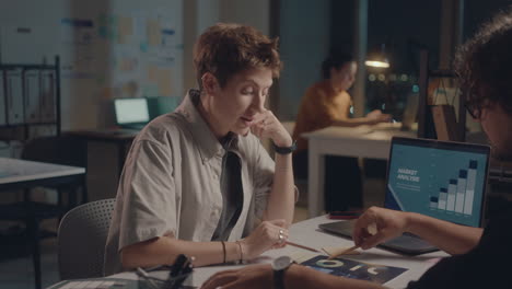 colleagues discussing business charts in office at night