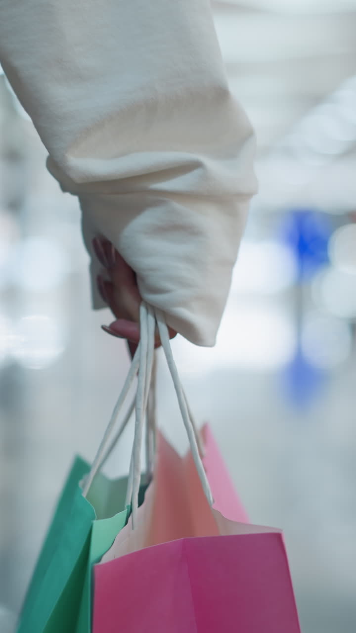 누군가의 손에 인 분홍색 쇼핑 가방, 민트색 가방과 함께, 다채로운 반사, 현대적인 소매 디스플레이를 특징으로하는 활기찬 쇼핑몰 배경에 설정