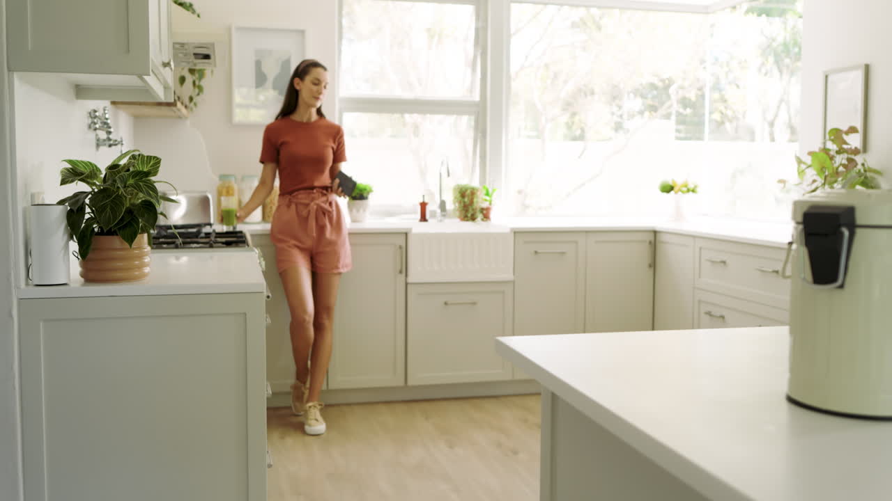 Donna sorridente in cucina che usa lo smartphone, godendosi il tempo libero a casa.