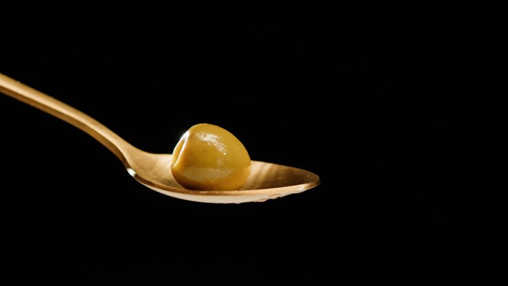 Olive oil poured onto an olive on a golden spoon