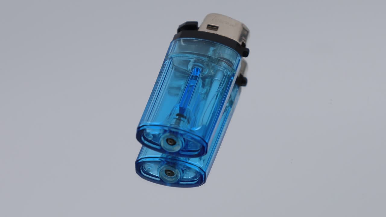 Transparent blue plastic lighter placed on a mirror surface, rotating and creating a clear reflection of its shape and details