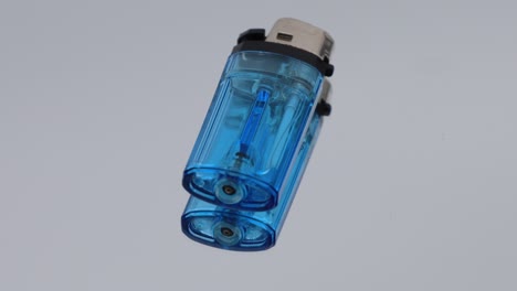 transparent blue plastic lighter placed on a mirror surface, rotating and creating a clear reflection of its shape and details