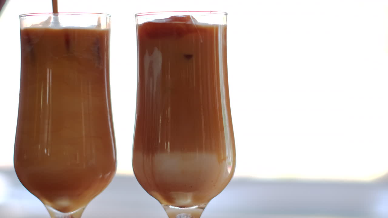 Due iced latte in bicchieri alti mescolati al rallentatore