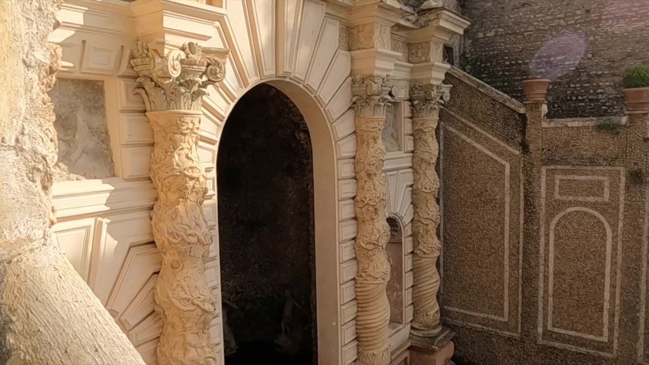 Una panoramica a destra rivela una fontana in pietra con testa di leone consumata dal tempo contro ornate colonne barocche e antiche mura a Tivoli vicino a Roma