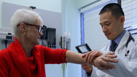 Vista-Lateral-De-Un-Joven-Médico-Asiático-Examinando-A-Un-Paciente-Mayor-Con-Lupa-En-La-Clínica