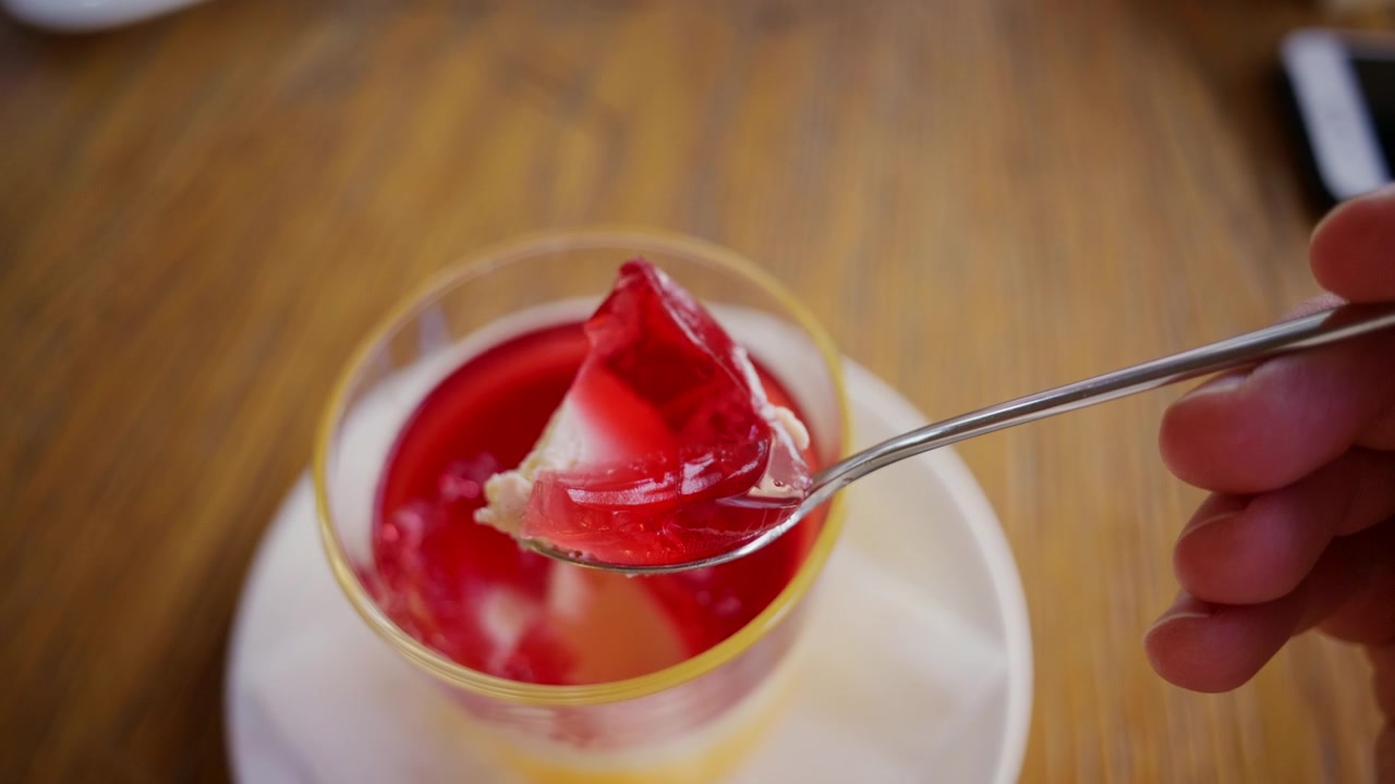 Primo piano di un cucchiaio che solleva un pezzo di gelatina di frutta rosso vivo da una coppetta da dessert di plastica trasparente.